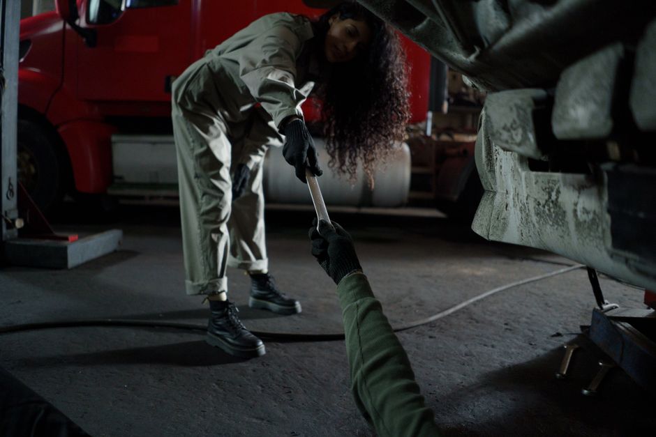 A mechanic handing a wrench in a dimly lit garage workshop, showing teamwork in auto repair.