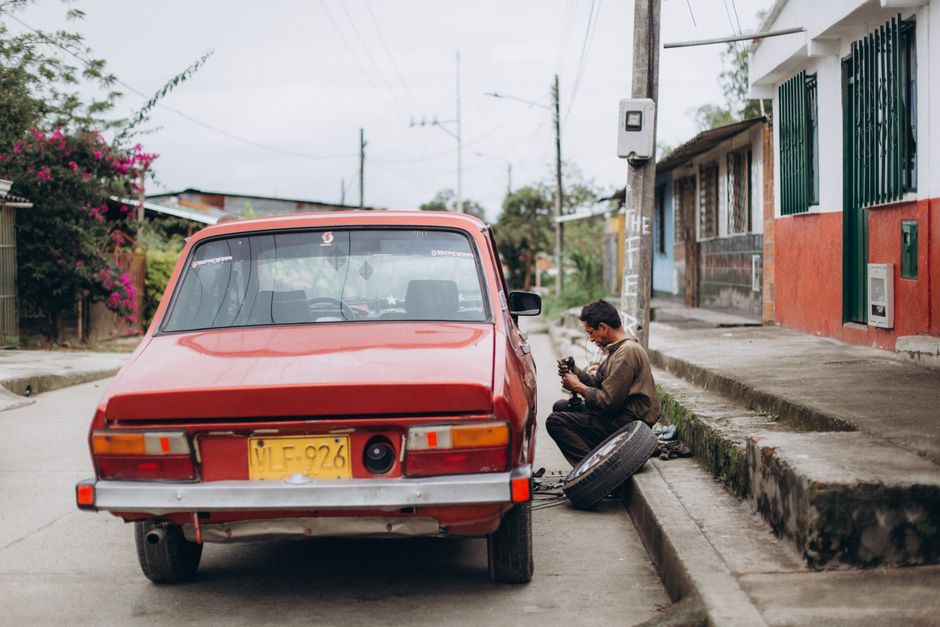 Mechanic repairing a red car on a street side in an urban neighborhood. Manual work in action.