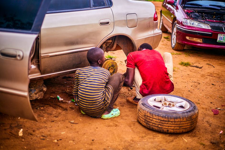 Two men fixing a car tire on a dirt road in Kaduna, Nigeria. Automotive repair scene.